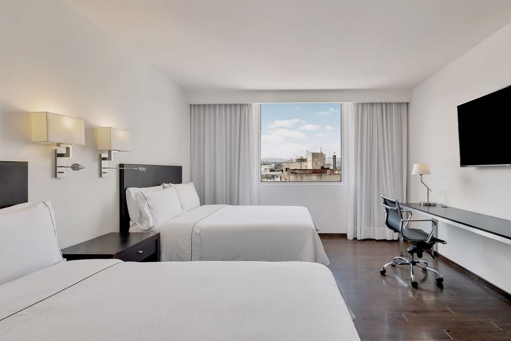 TV con escritorio de trabajo frente a la cama junto a la ventana, y piso de madera en la habitación de Fiesta Inn