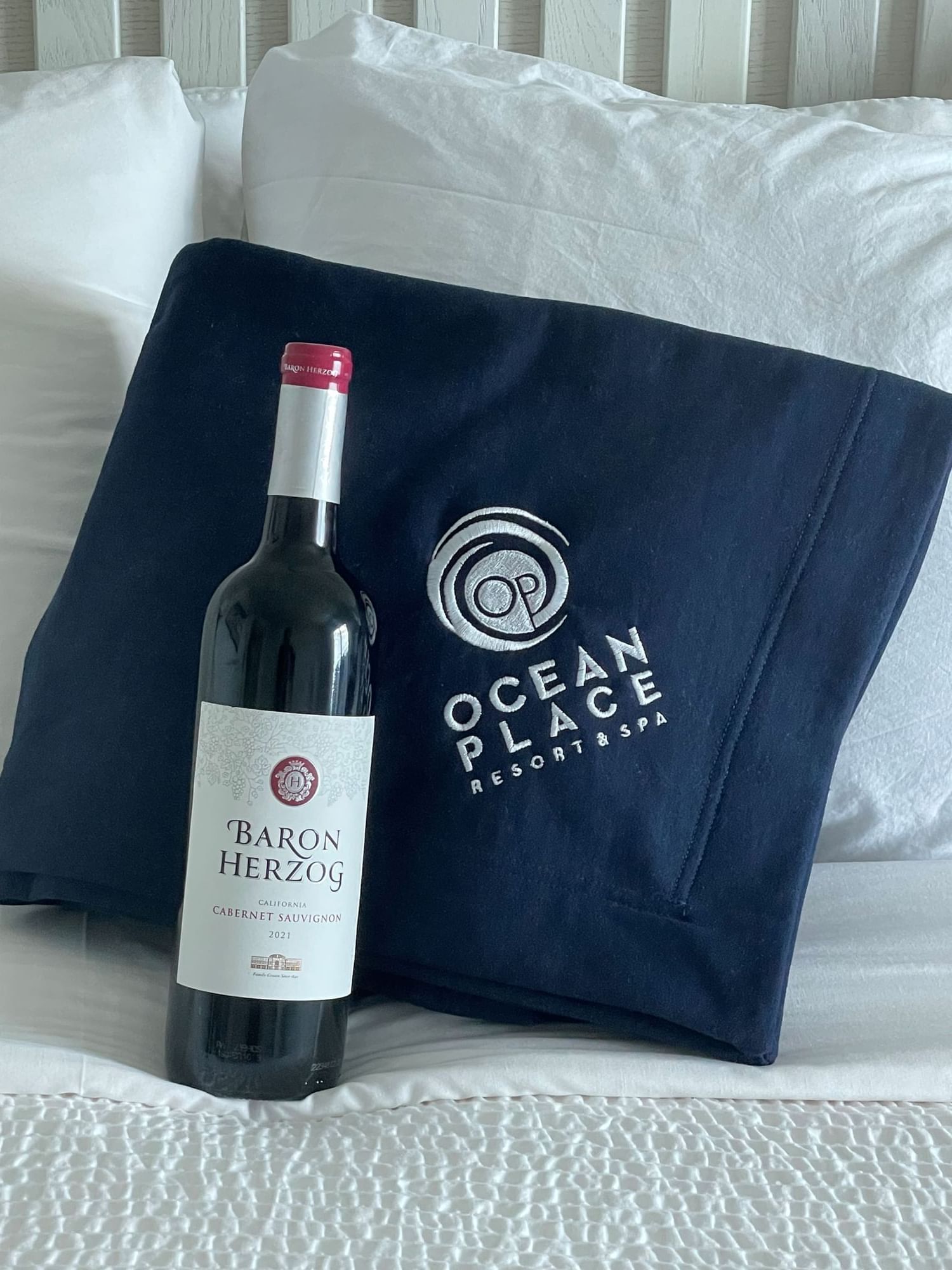 Bottle of wine and navy OP blanket folded on the bed 