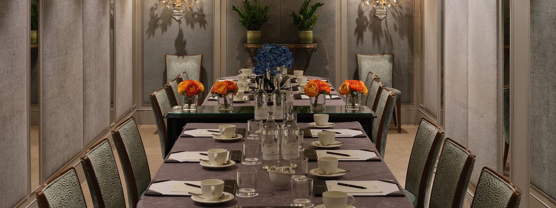 Long dining table with tea sets by plush chairs under ornate sconces, in Cadogan Suites at Warwick Hotels & Resort