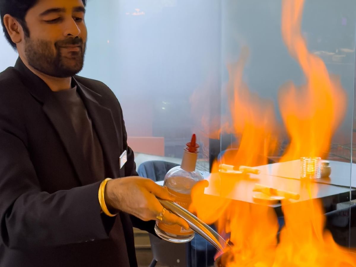 Man holding a flaming torch and a bottle of liquor at Minnoz Restaurant + Lounge in Nanaimo at Coast Bastion Hotel.