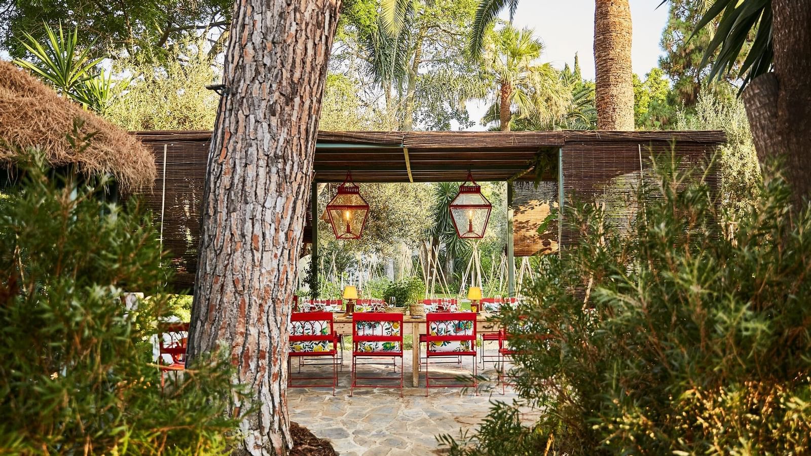 Outdoor dining with red patterned chairs under a shaded pergola surrounded by rosemary at Marbella Club