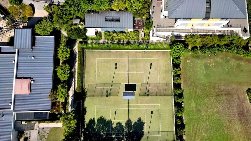 Aerial view of a tennis court between buildings and greenery near Mercure Kooindah Waters