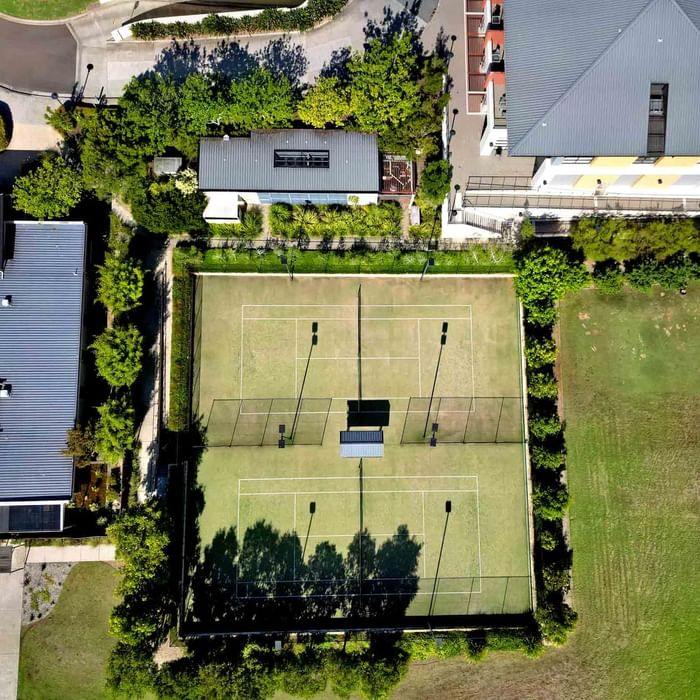 Aerial view of a tennis court between buildings and greenery near Mercure Kooindah Waters