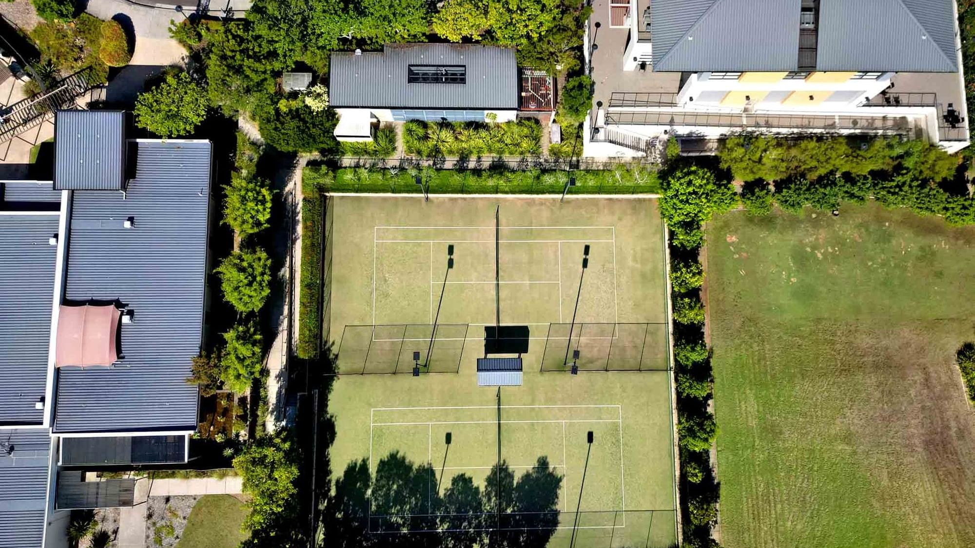 Aerial view of a tennis court between buildings and greenery near Mercure Kooindah Waters