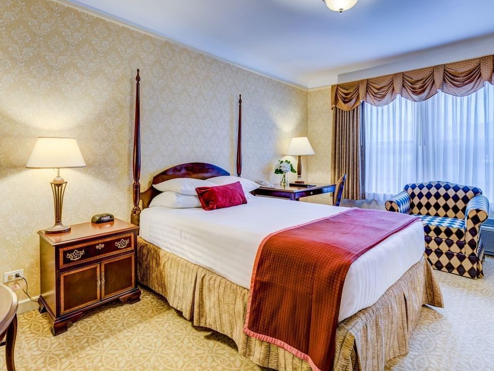 Queen bed with bedside lamps and a patterned chair in standard room at The Carleton of Oak Park Hotel