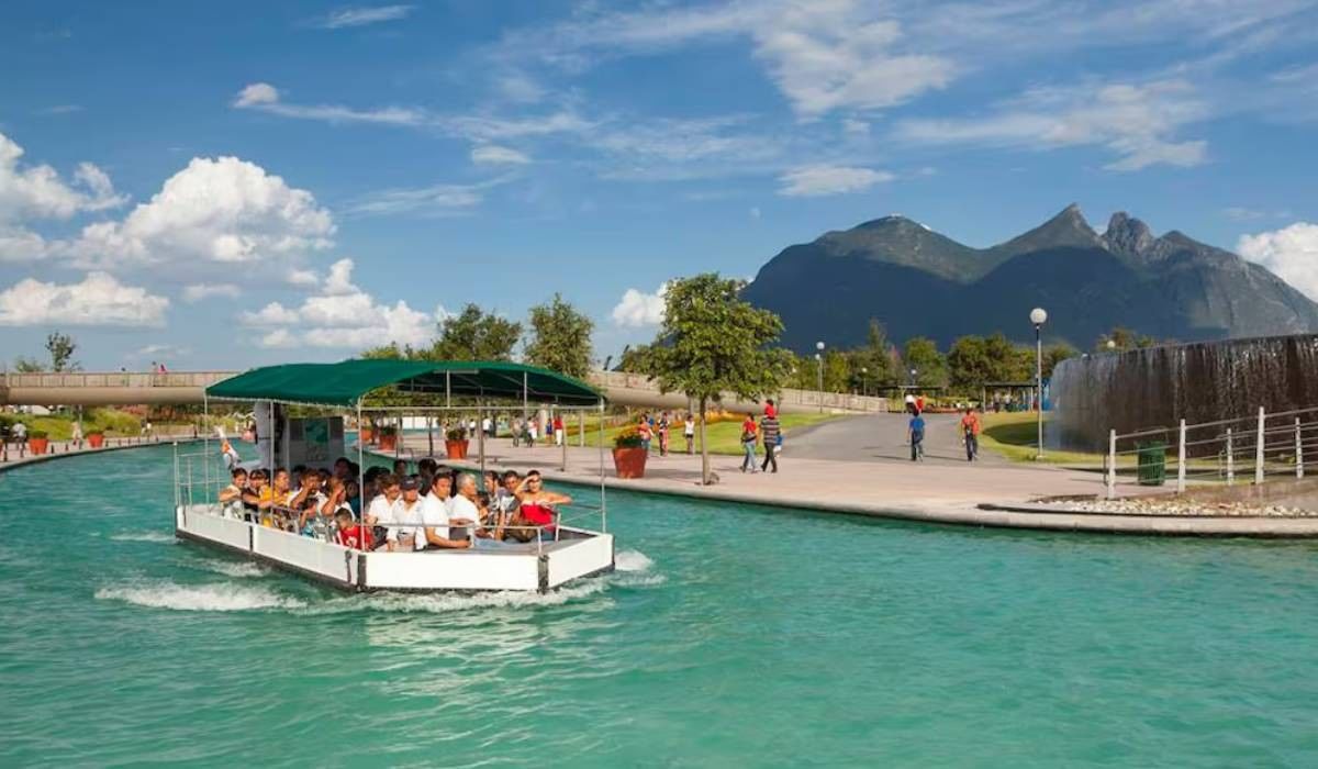 Tour boat in a turquoise canal by a walkway under a blue sky and mountain peaks at Camino Real Pedregal Mexico
