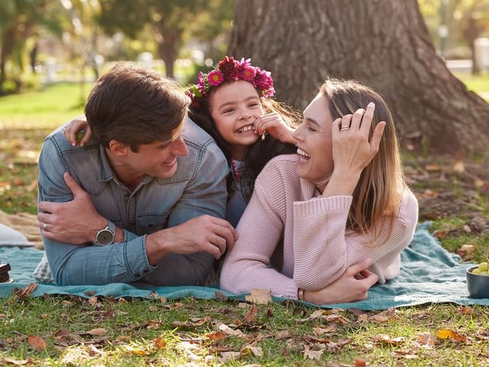 A family of three lying on a blanket in a park