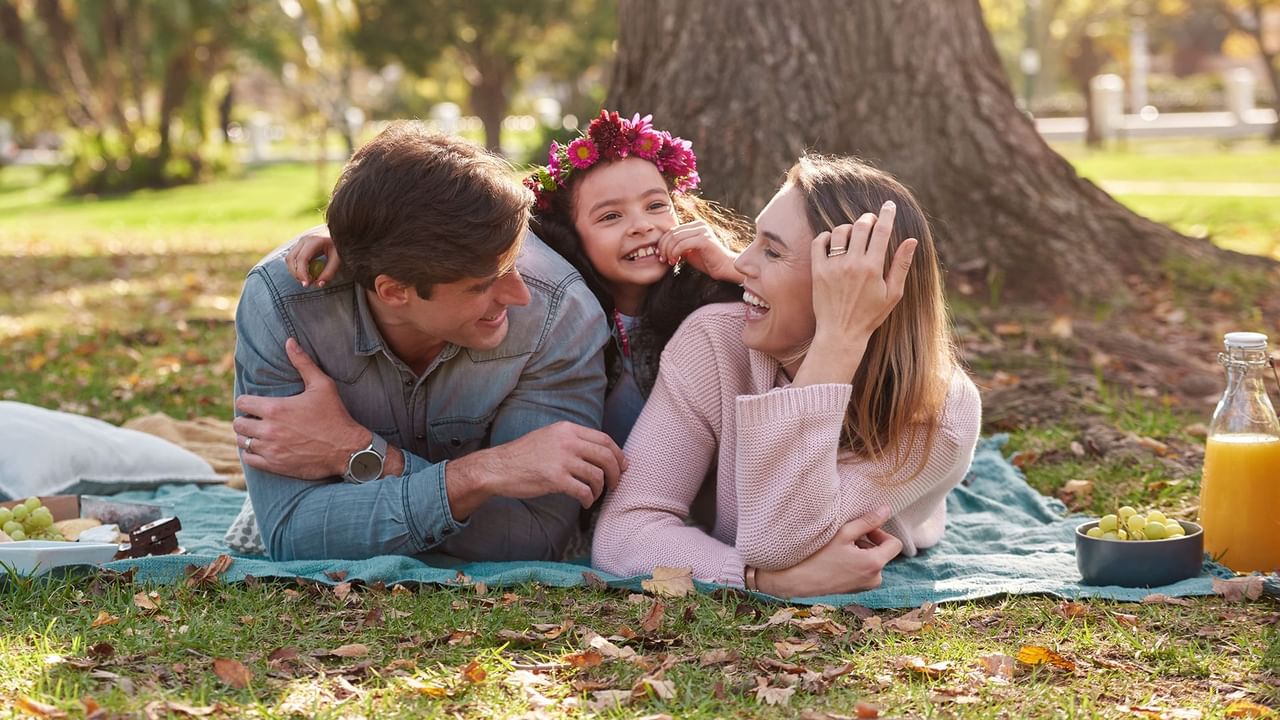 A family of three lying on a blanket in a park