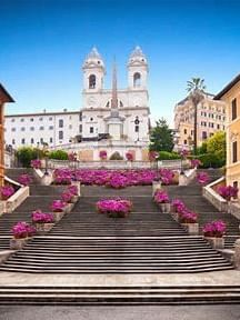 A beautiful view of the Spanish Steps adorned with vibrant pink flowers under a blue sky near Rome Luxury Suites