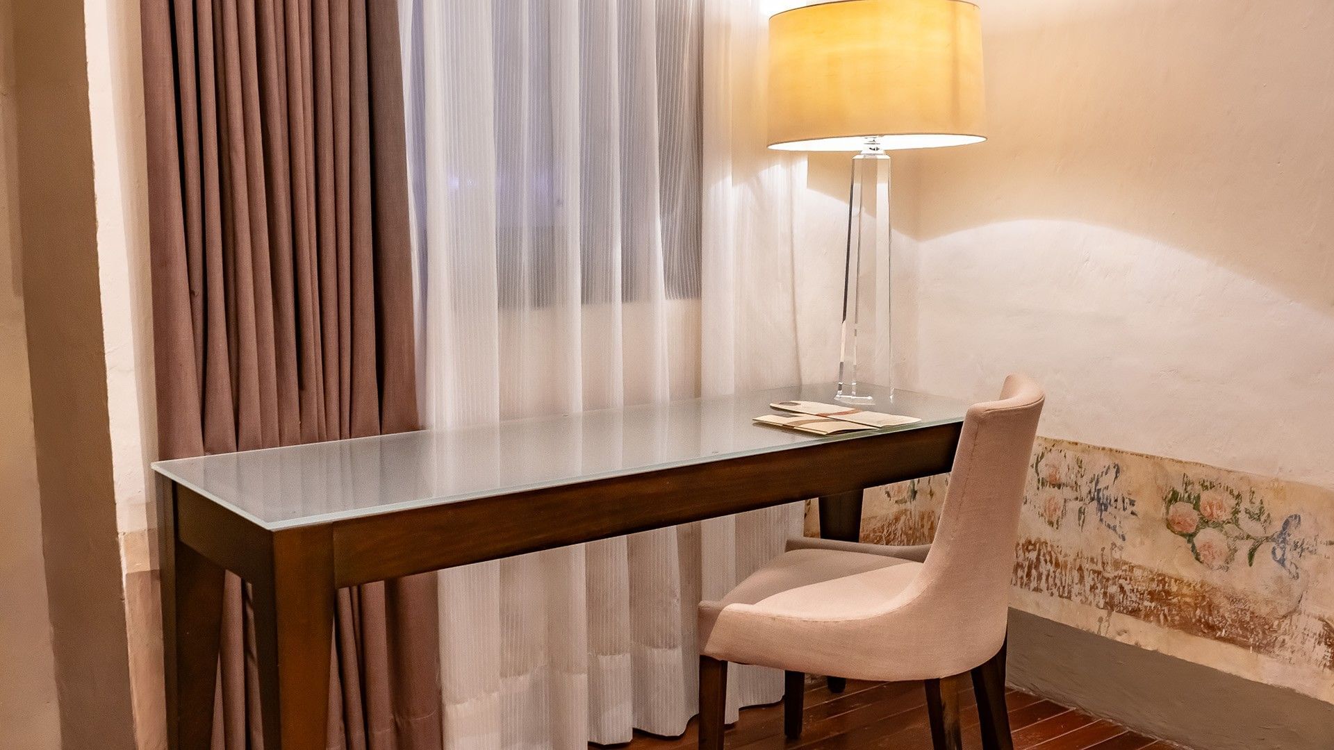 A minimalist glass desk, tan chair, and modern crystal lamp with a glow in King Novicia at Quinta Real Puebla