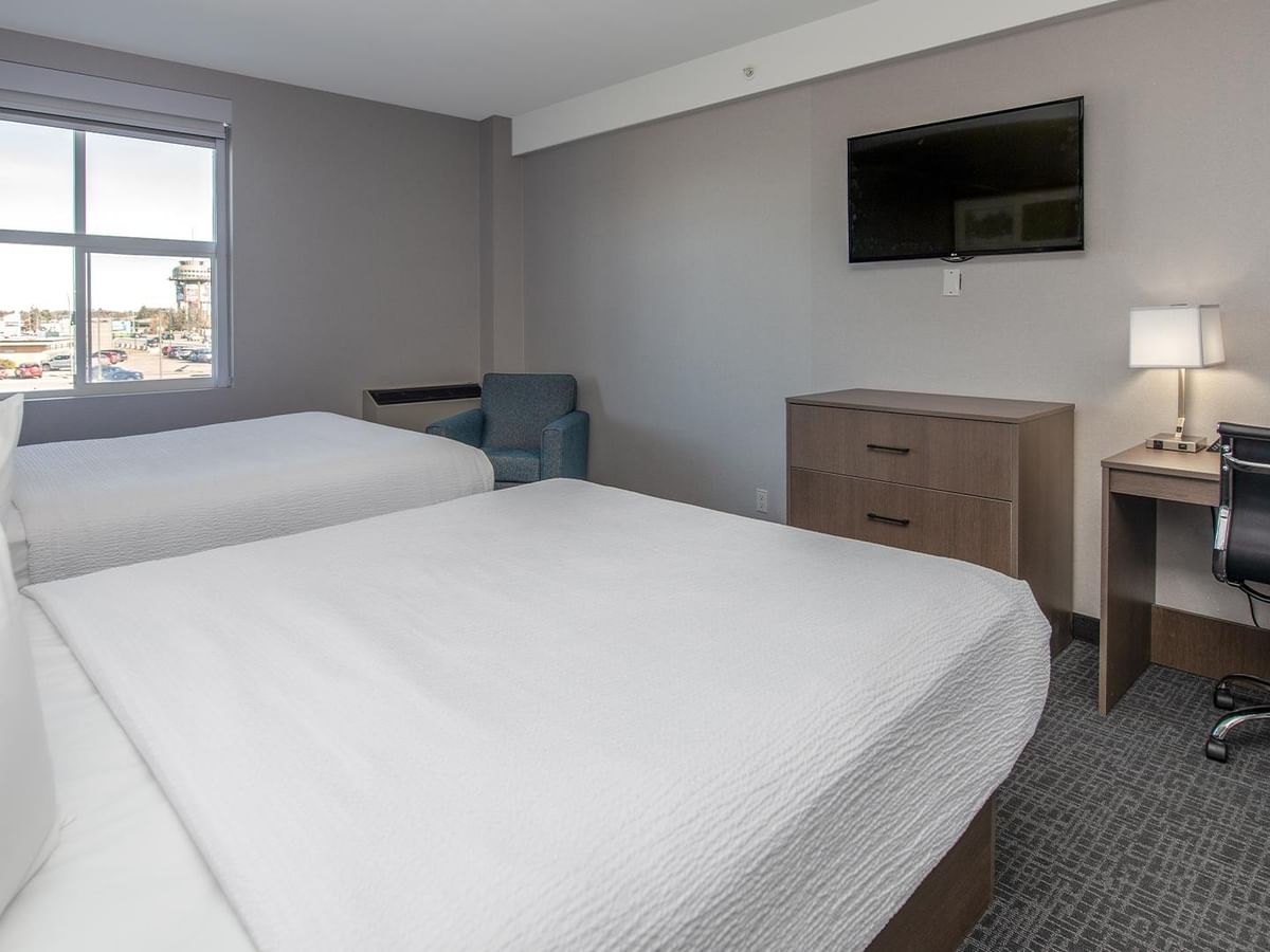 Two queen beds, desk, chair, TV, and window in a room.