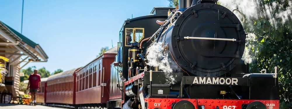 Vintage AMAMOOR steam train with red passenger cars at a sunny station near the Novotel Sunshine Coast Resort