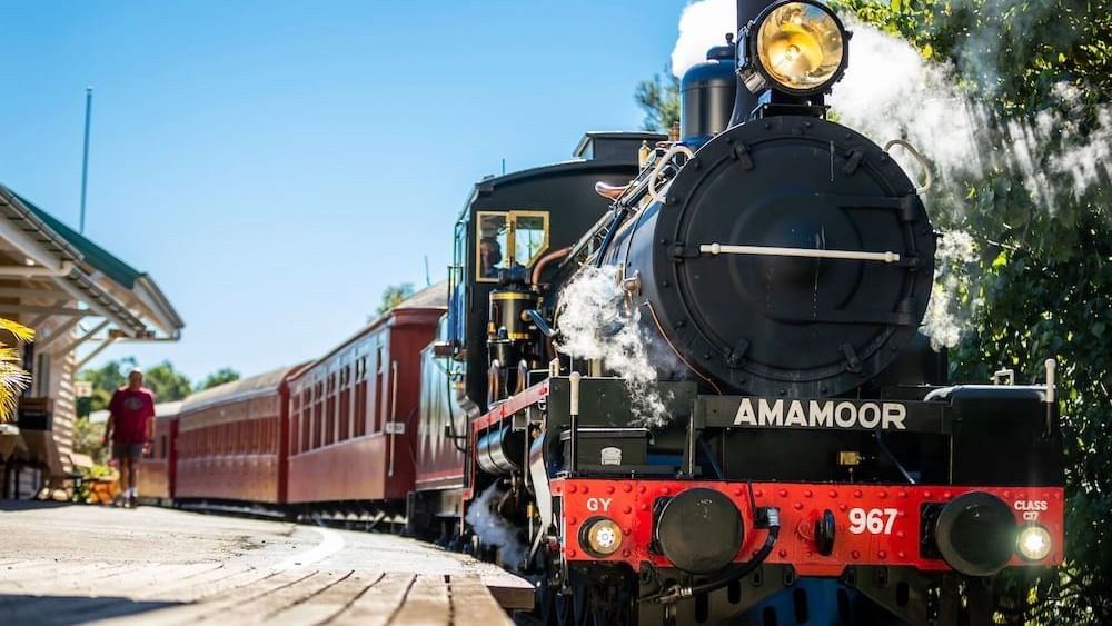 Vintage AMAMOOR steam train with red passenger cars at a sunny station near the Novotel Sunshine Coast Resort