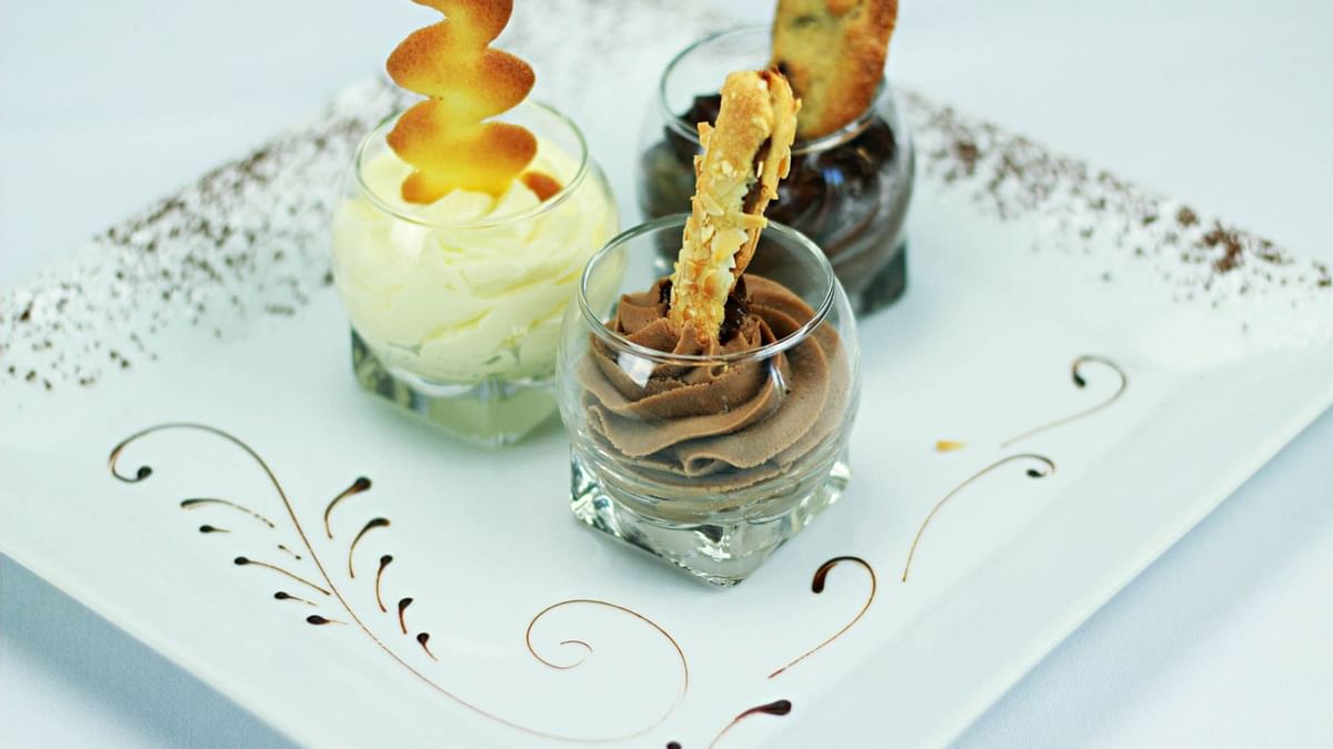 Trois verres de desserts variés sur une assiette décorée avec des biscuits et des motifs dorés.