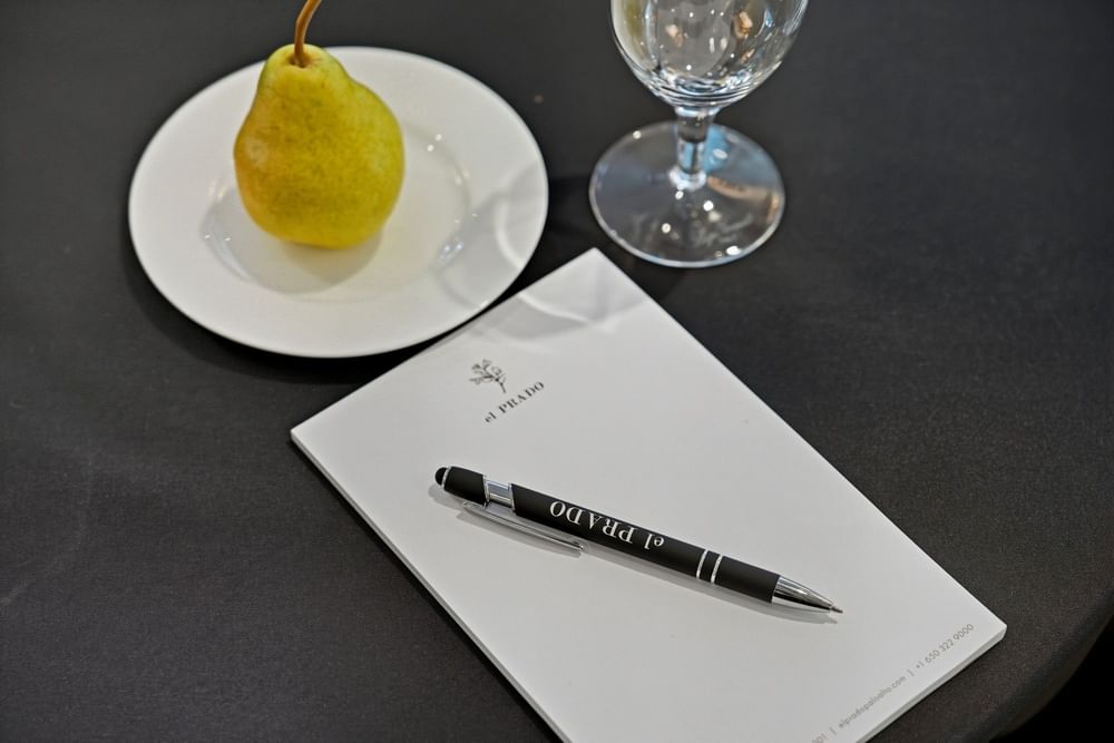 close up of meeting collateral featuring the el PRADO logo, and a yellow green pear on a white plate