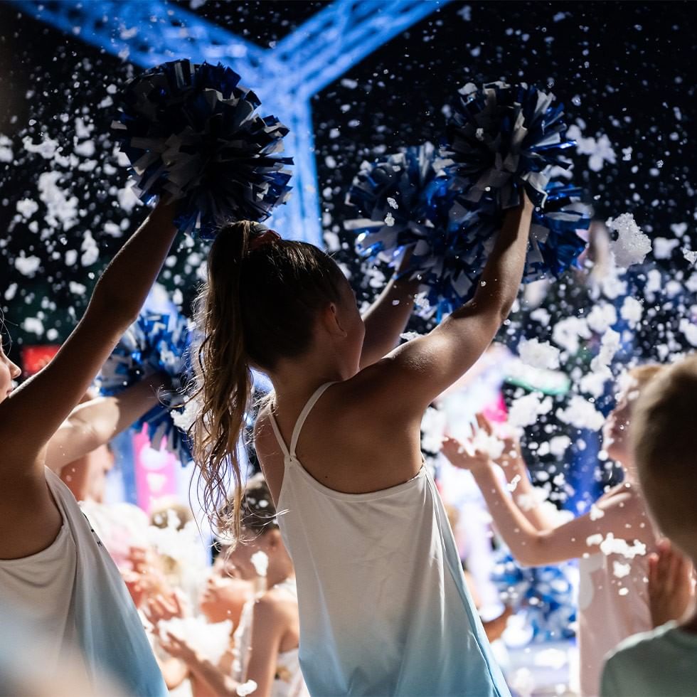 Ragazze con pompon blu e bianchi che si esibiscono in uno spettacolo con la folla.