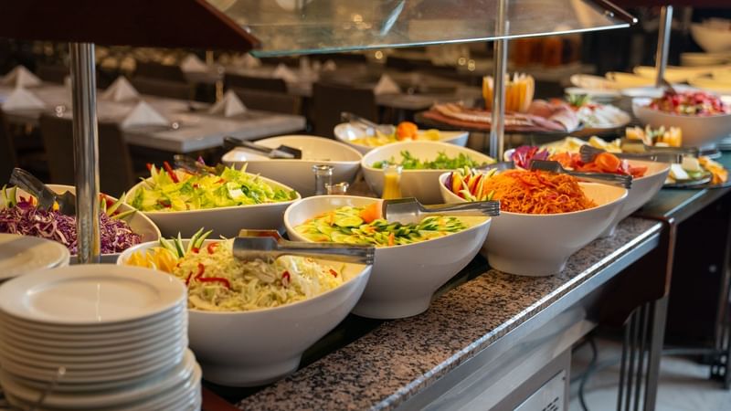 White bowls with various salad options and tongs at a buffet setting at Saja by Warwick Madinah in Madinah.