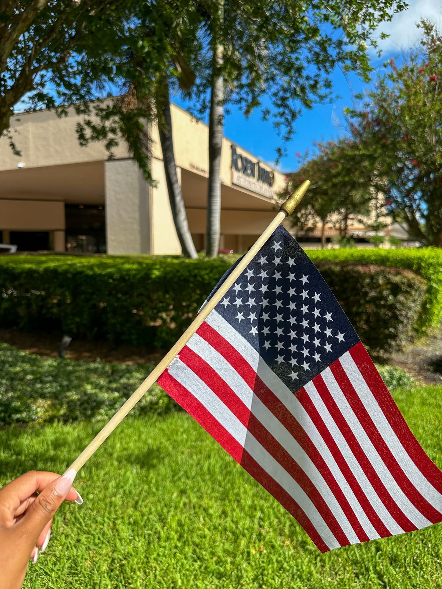 A hand holding an American flag with an out of focus Rosen Inn hotel in the background.