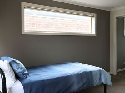 A cozy bedroom with a blue bed, gray walls, and a large window at La Trobe University Regional Housing – Melton.