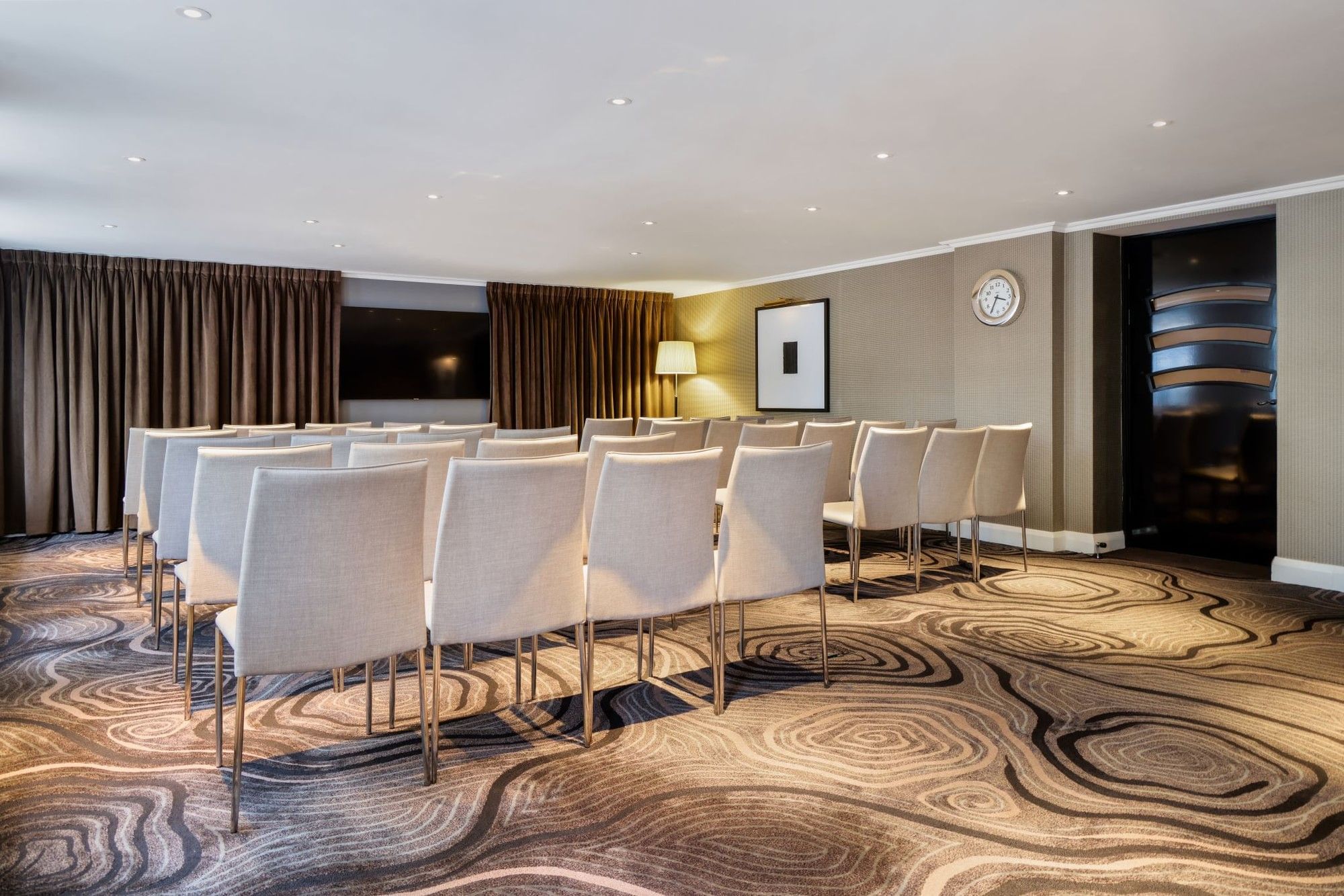 Theater-style set up facing a wall-mounted TV in an event room at The May Fair Hotel