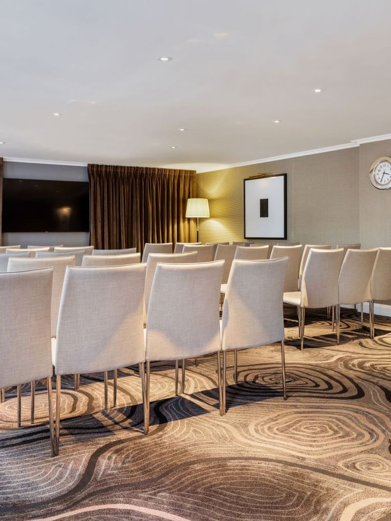 Theater-style set up facing a wall-mounted TV in an event room at The May Fair Hotel
