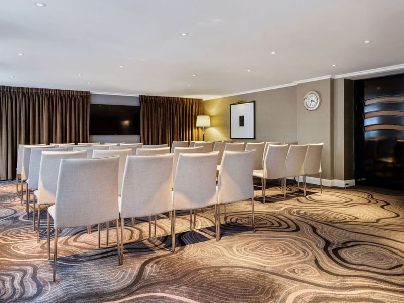 Theater-style set up facing a wall-mounted TV in an event room at The May Fair Hotel