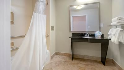 ADA King Room bathroom with a white shower curtain by a black vanity under a mirror at Galleria Palms Hotel