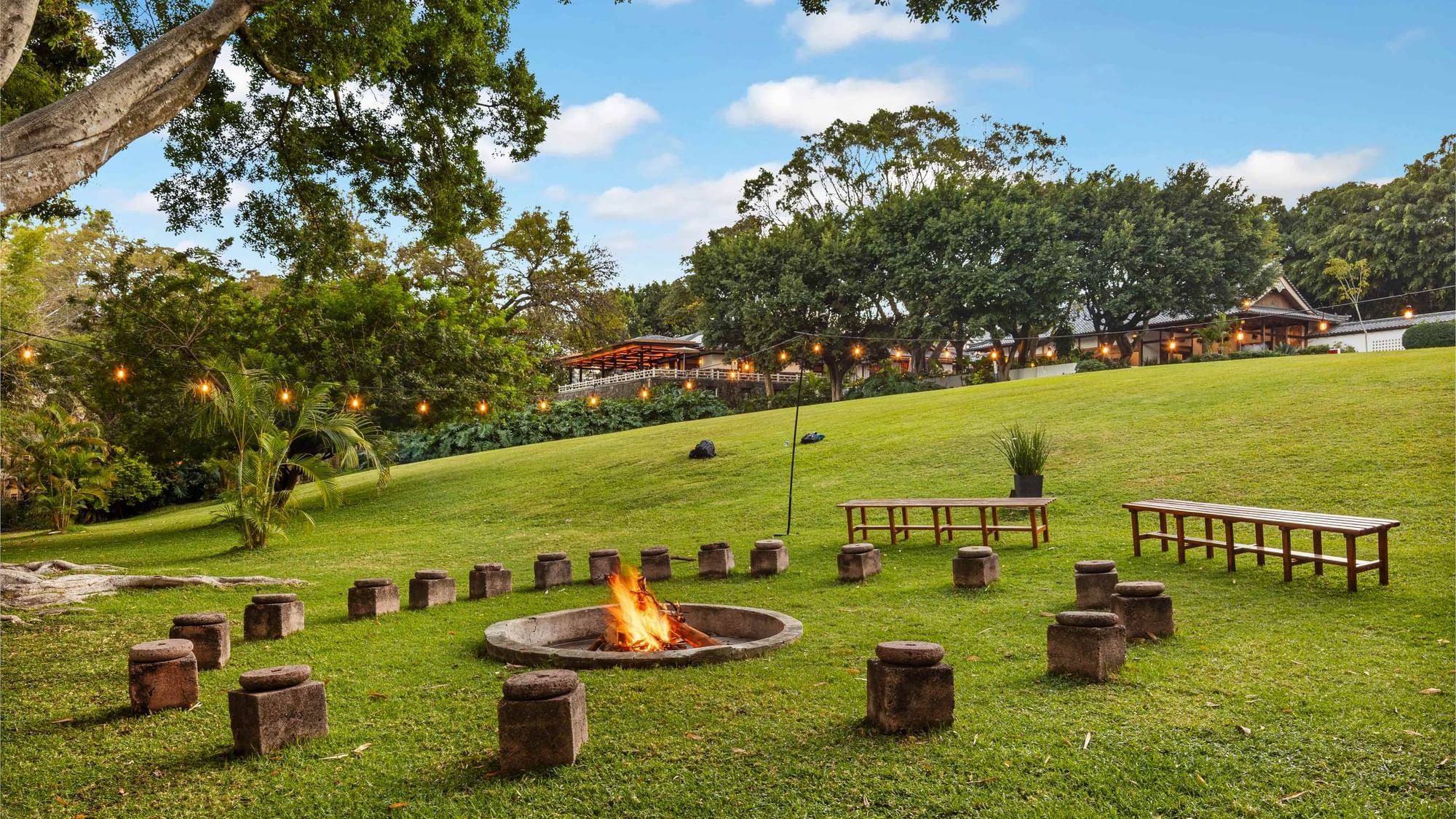 Bonfire surrounded by stone seating and tables on grassy field with lights at Grand Fiesta Americana Sumiya Cuernavaca.