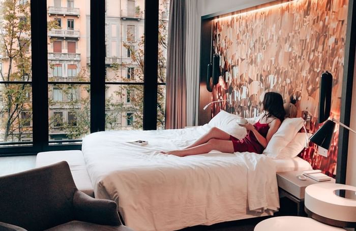 Donna rilassata sul letto in una camera elegante con vista su edificio e alberi da DUPARC Contemporary Suites