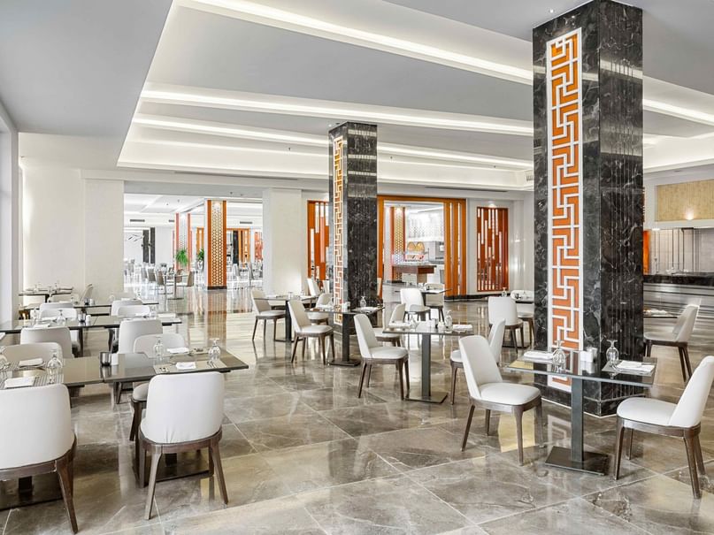 Ein elegantes Restaurant mit weißen Tischen und Stühlen, dekorierten Säulen und großem Fenster.