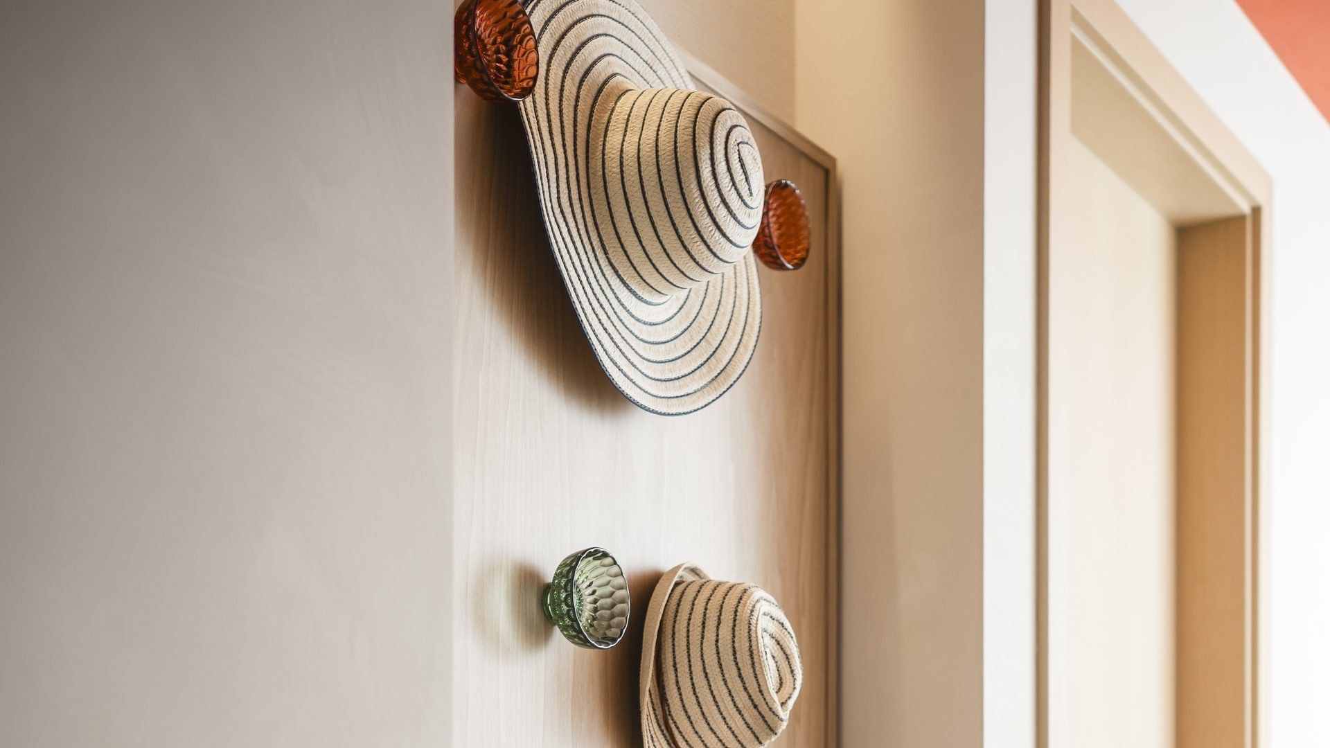 Cappello di paglia appeso a un gancio su una porta con un altro cappello sotto.