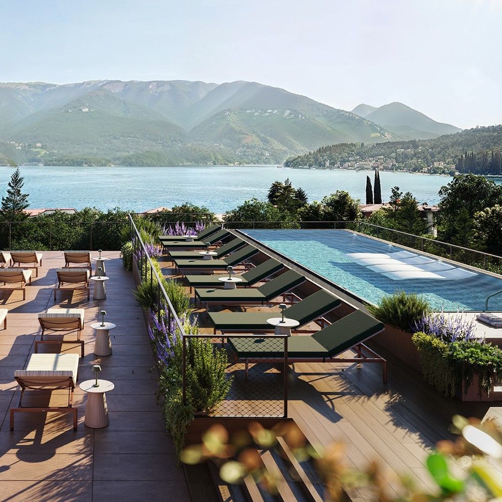 An outdoor pool with lounge chairs and a view of the lake and mountains.