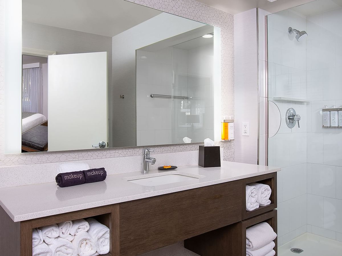 A clean bathroom with a vanity, sink, mirror, folded towels, and a glass shower enclosure.