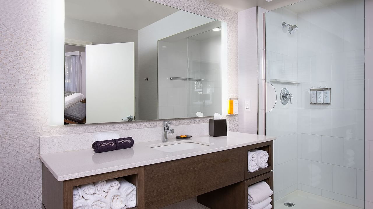A clean bathroom with a vanity, sink, mirror, folded towels, and a glass shower enclosure.