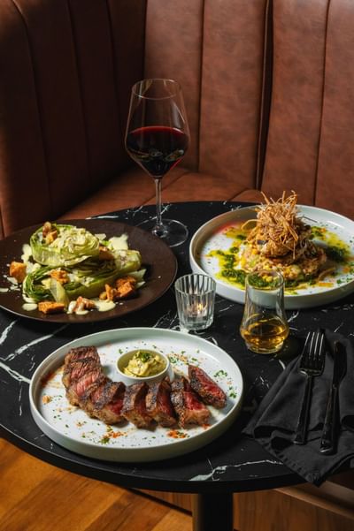 Elegant dining setup with a stylish steak dish, romaine salad, seafood plate, and red wine at Cypress & Oak