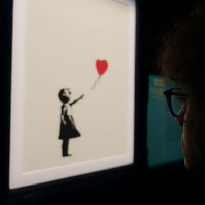 A person wearing glasses looks at a framed artwork of a girl in a dress holding a balloon.