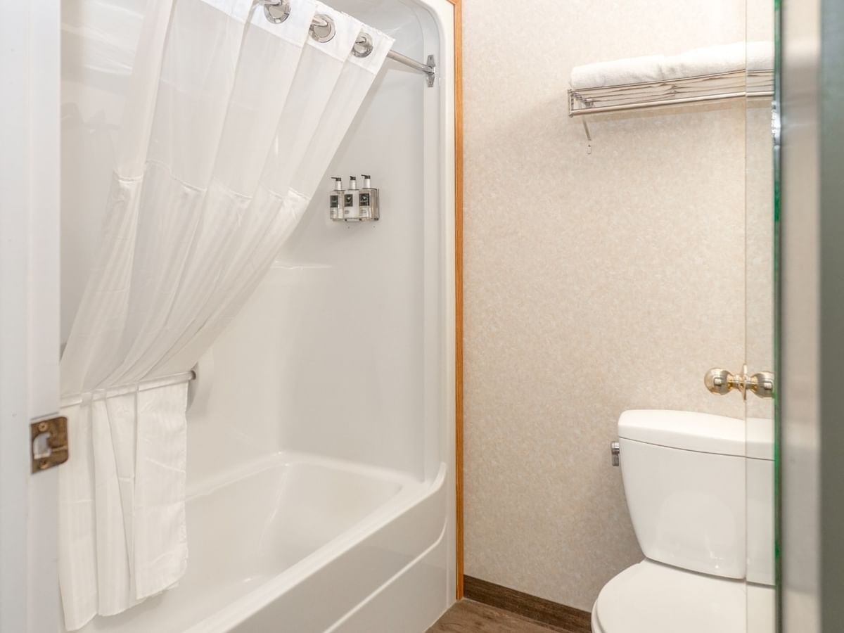 White shower with curtain, toilet, and towel rack in a small bathroom.