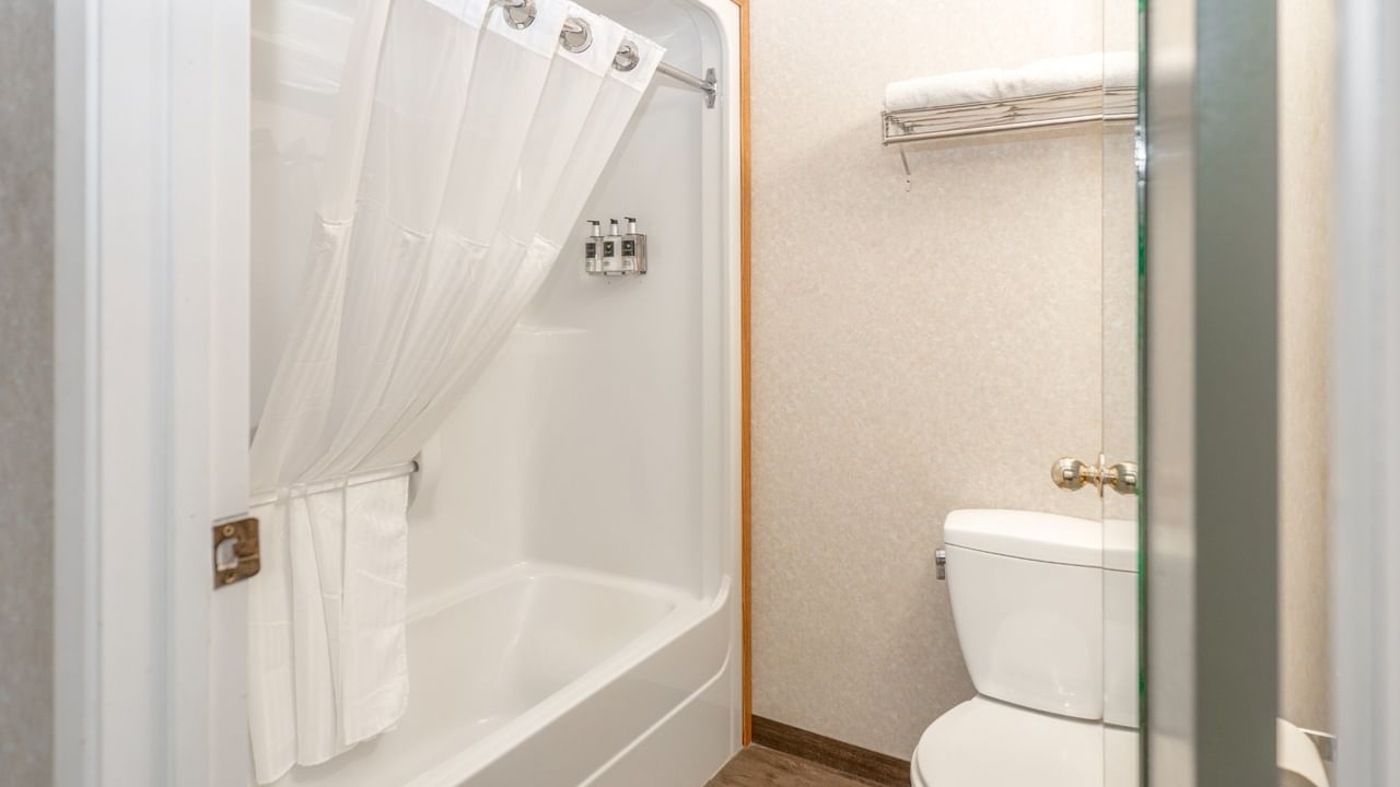 White shower with curtain, toilet, and towel rack in a small bathroom.