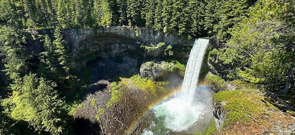 View of Brandywine Falls cascading into a forested canyon, with a rainbow forming in the mist below.