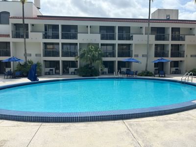 Curved pool with turquoise water facing hotel room balconies and blue umbrellas along the courtyard at Miami Lakes Hotel