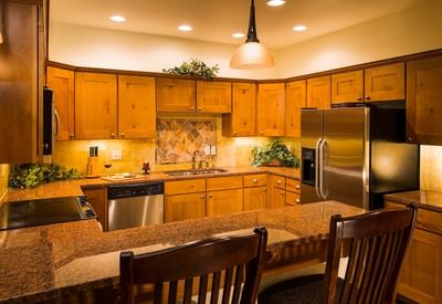 A full kitchen at The Stanley Hotel with wooden cabinets, granite countertops, and a breakfast bar with two chairs