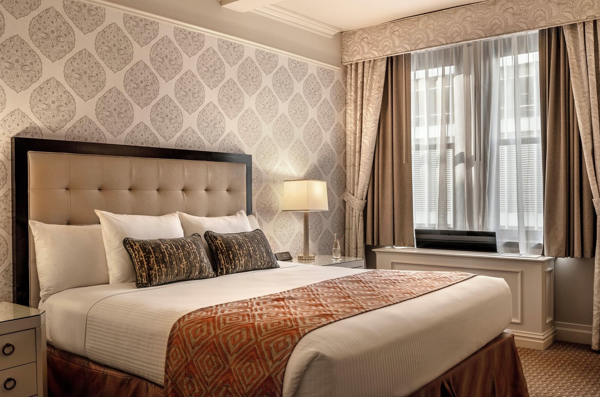 King bed against ornate damask wallpaper and table lamp in On the Avenue One Bedroom Suite at Warwick New York