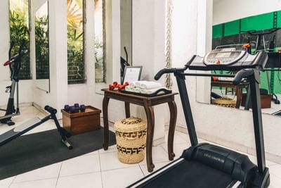 Treadmill and dumbbells by a wooden table with rolled towels under mirrors in the gym at Hotel Montana Haiti