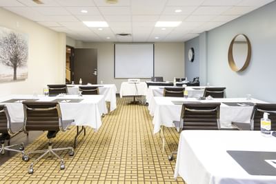 Bright conference room with white tablecloths on desks, black rolling chairs and a projector screen at Rodd Royalty