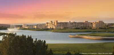 Hilton Santa Fe Buffalo Thunder resort at sunset, with a calm lake, golf course, and fountain in the foreground