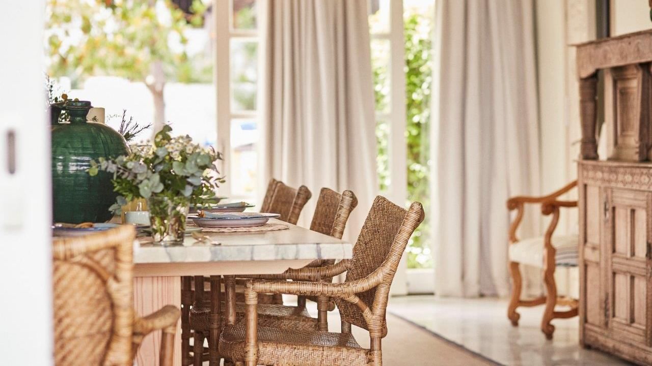 Villa del Mar dining room with a marble table, wicker chairs, & large windows overlooking the garden at Marbella Club