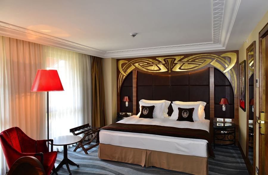 Red velvet chairs by a small table surrounding a bright window in Deluxe Room at Warwick Ankara