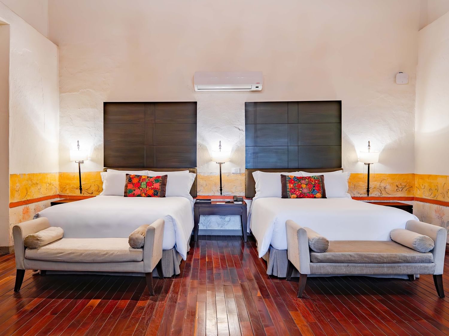 Two double beds with colorful blankets and benches in a Superior room at Quinta Real Puebla in Heroica Puebla de Zaragoza.