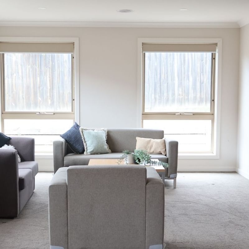 Living room with two couches, TV, and windows at La Trobe University Regional Housing – Melton.