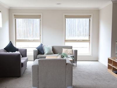 Living room with two couches, TV, and windows at La Trobe University Regional Housing – Melton.